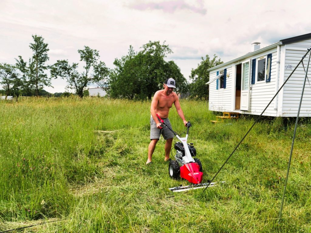 Über uns 2 Marek im Garten mit Balkenmäher und Mobilehome im Hintergrund